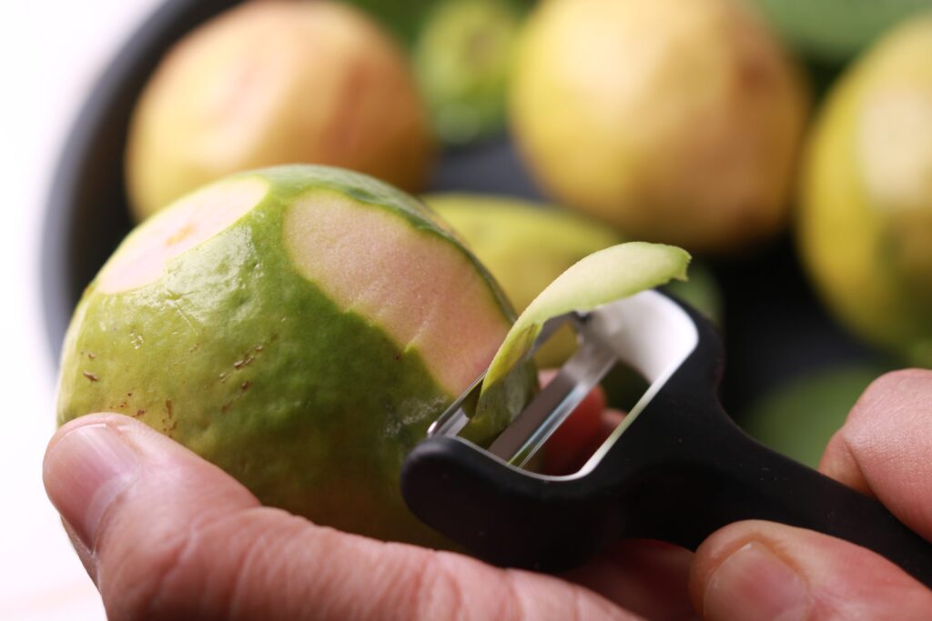 A guava being expertly peeled, revealing its juicy flesh for cooking